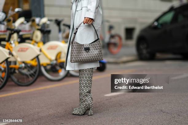 Guest wears a pale gray leather belted trench coat, a black and white monogram print pattern fabric shoulder bag from Salvatore Ferragamo, black and...