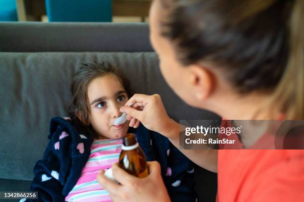 ein kind mit einer erkältung nimmt medikamente. mutter gibt dem kind medizin - homeopathic medicine stock-fotos und bilder
