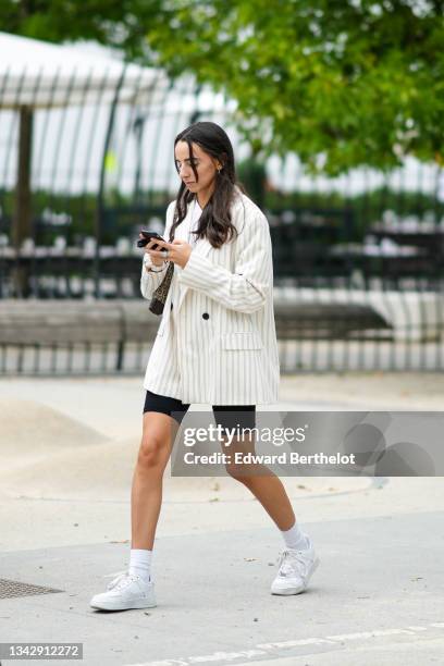 Guest wears silver earrings, a white t-shirt, a white with black small stripes oversized blazer jacket, a beige and brown FF monogram shoulder bag...