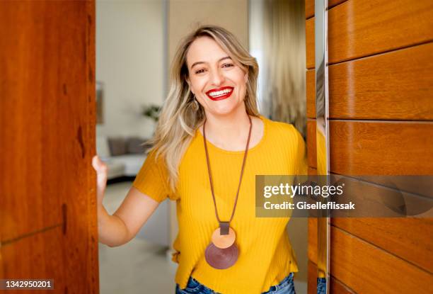 smiling woman standing at the open front door of her home - door greeting stock pictures, royalty-free photos & images