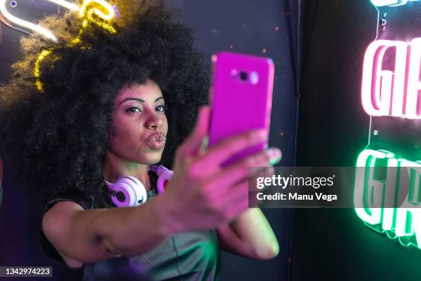 an afro-caribbean woman takes a selfie with some neon lights next to it. - egoismus stock-fotos und bilder