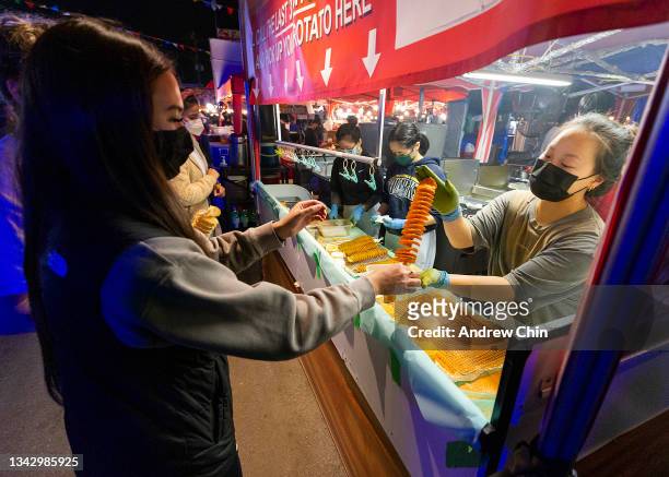 Woman wearing a protective face mask receives her rotato potato stick from a food vendor at Richmond Night Market on September 25, 2021 in Richmond,...