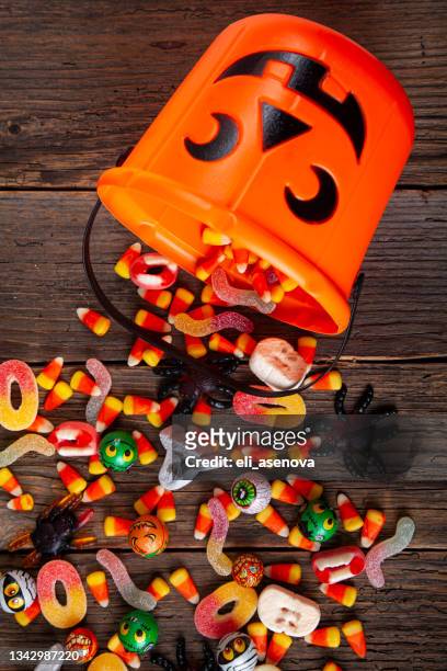 halloween jack o lantern pail with bottom border of spilling candy over brown rustic wood - candy corn stock pictures, royalty-free photos & images