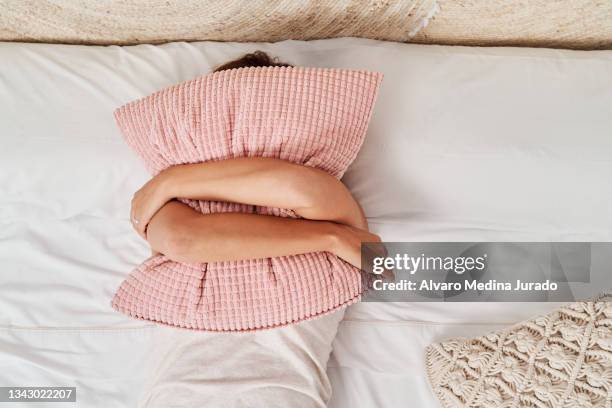 top view of a beautiful young woman lying in bed covering her face with a pillow. - deitando - fotografias e filmes do acervo