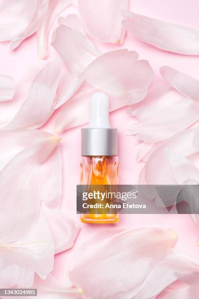 the glass bottle with cosmetic liquid placed on petals of flowers on a pink background. concept of body care. flat lay style - argan oil stock-fotos und bilder