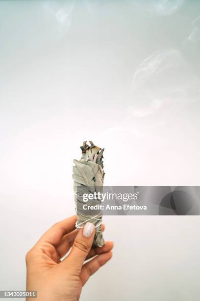 woman is holding in a hand smoldering white sage on gray background. process of room fumigation ritual. copy space for your design. front view - sage background stock pictures, royalty-free photos & images