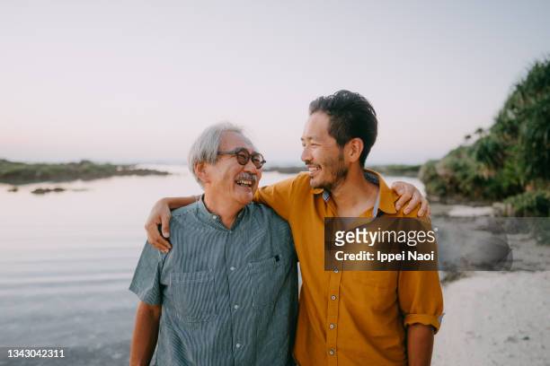 senior father and adult son having a good time on beach at sunset - hijo adulto fotografías e imágenes de stock