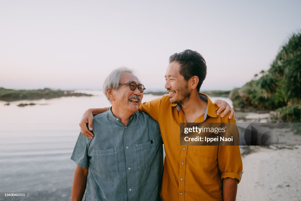 Senior father and adult son having a good time on beach at sunset