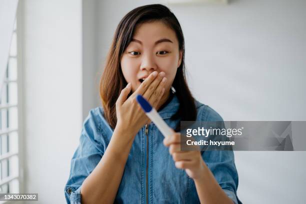 excited asian woman holding and looking at pregnancy test kit - pregnancy test stock pictures, royalty-free photos & images