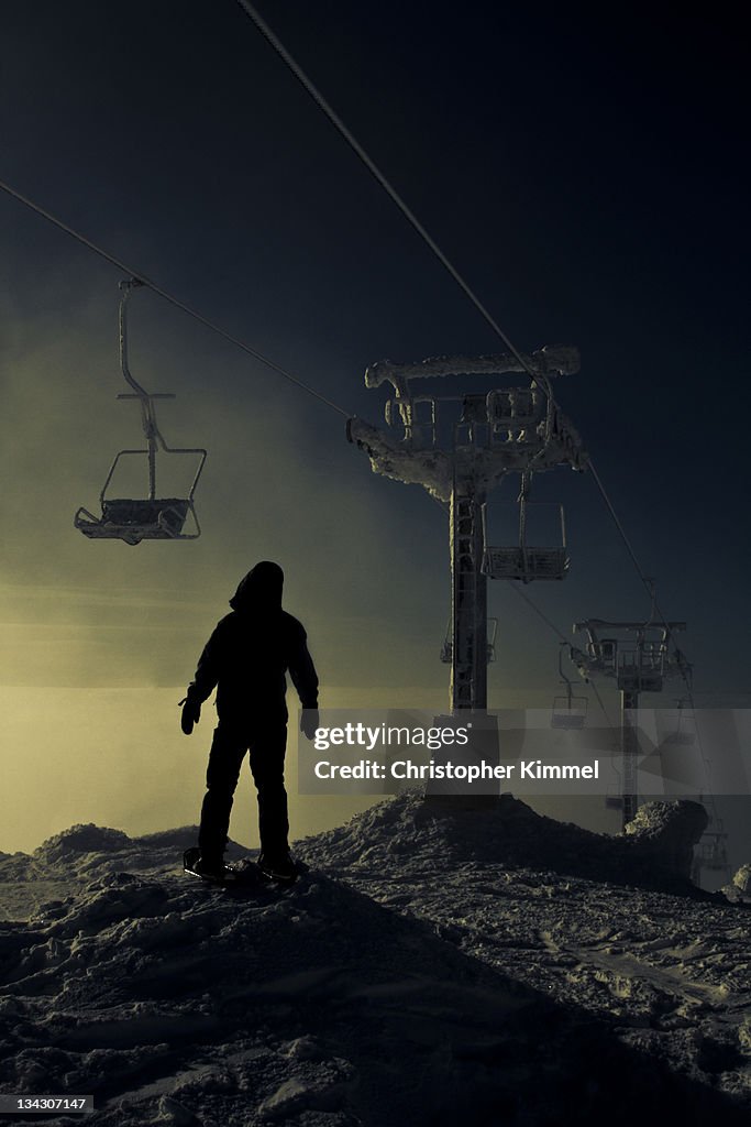 Silhouetted person stands below ski hill Chairlift