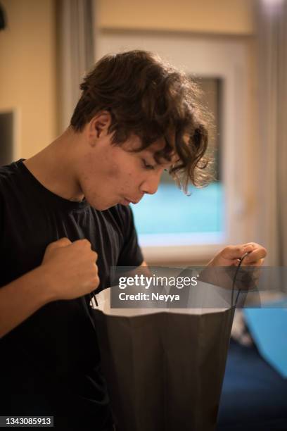 curious teenager boy looking into a black paper bag - teenager boy shopping bildbanksfoton och bilder