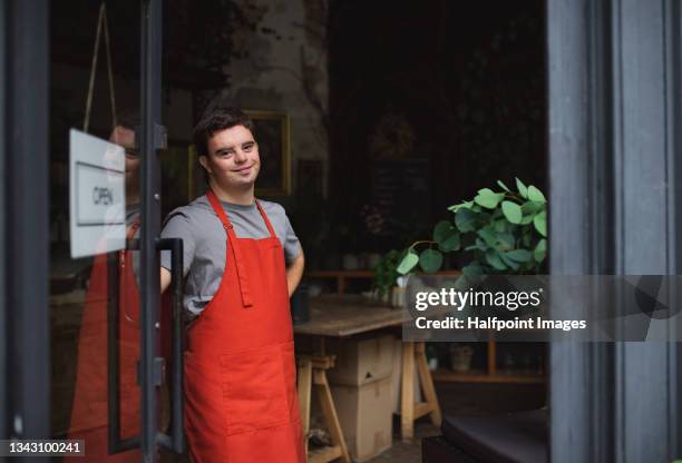 young male florist with down syndrome standing indoors in flower shop, looking at camera. - human rights work stock pictures, royalty-free photos & images
