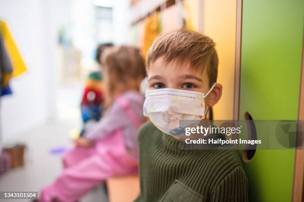 pre school boy with face mask sitting indoors in cloakroom at nursery, coronavirus concept. - young boys changing in locker room fotografías e imágenes de stock