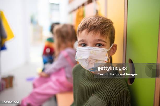 pre school boy with face mask sitting indoors in cloakroom at nursery, coronavirus concept. - young boys changing in locker room 個照片及圖片檔