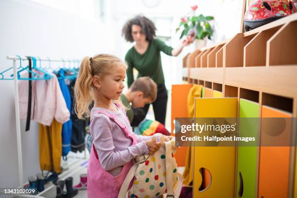 pre school children with teacher putting clothes into lockers in cloakroom in nursery. - preschool student stock pictures, royalty-free photos & images