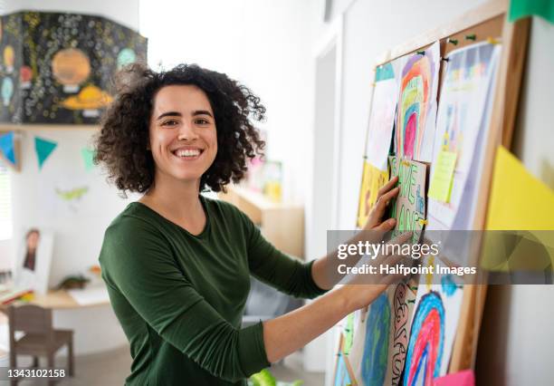 preschool teacher making bulletin board indoors at nuresry school, smiling and looking at camera. - teacher pre school imagens e fotografias de stock