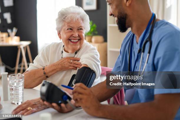 happy healthcare worker or caregiver visiting senior woman indoors at home, measuring blood pressure. - medicare fotografías e imágenes de stock