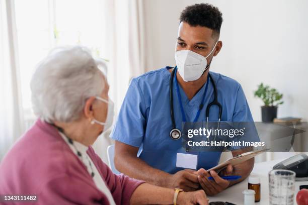 happy healthcare worker or caregiver with face mask visiting senior woman indoors at home, explaining. coronavirus concept. - 風邪マスク ストックフォトと画像