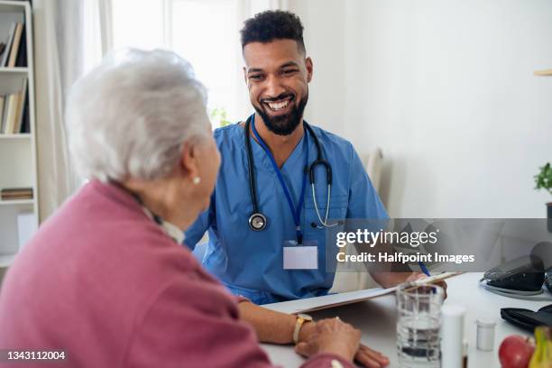 healthcare worker or caregiver visiting senior woman indoors at home, explaining. - asistencia de la comunidad fotografías e imágenes de stock