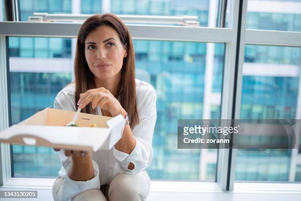 donna seduta in ufficio accanto alla finestra e mangiare da asportare fuori dalla scatola - lunch lady foto e immagini stock