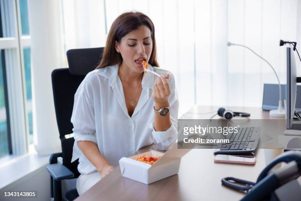 donna impegnata a fare una pausa pranzo alla sua scrivania, mangiando la pasta da avare - lunch lady foto e immagini stock