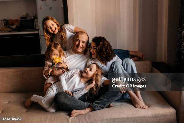 portrait of happy father, mother and three daughters on sofa at home - familia con tres hijos fotografías e imágenes de stock