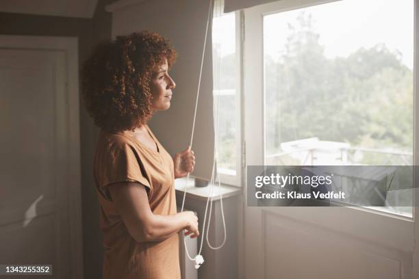 woman looking through window in bedroom - woman window home stock pictures, royalty-free photos & images