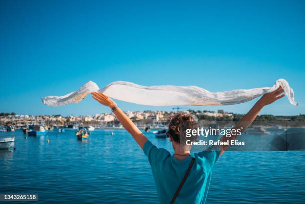 woman raising her foulard at the bay of water - marsaxlokk stockfoto's en -beelden