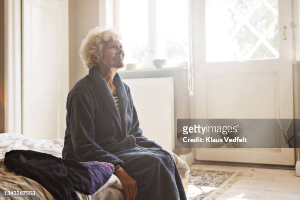 senior woman sitting on bed - woman in bathrobe stock pictures, royalty-free photos & images