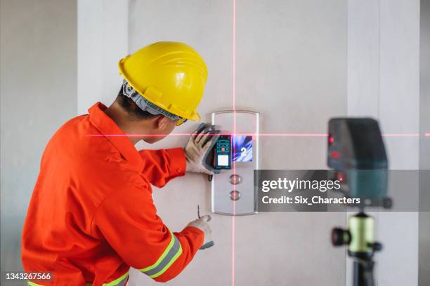 asian construction engineer in hardhat measuring wall with laser leveler next to elevator lift at construction site - waterpas stockfoto's en -beelden