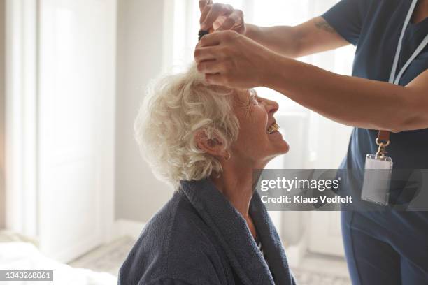 nurse combing smiling senior woman's hair - pflegedienst blau stock-fotos und bilder