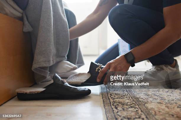female nurse helping senior man wearing shoe - alte schuhe stock-fotos und bilder