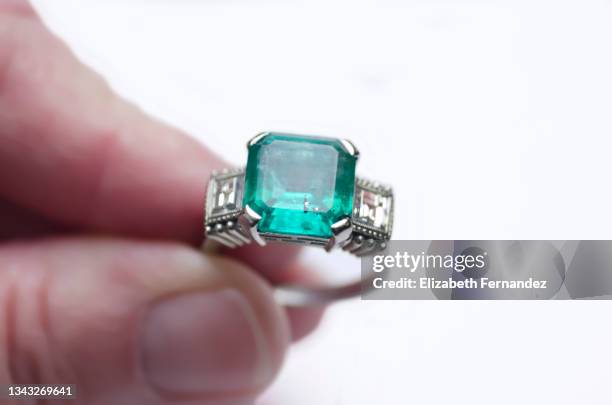 a woman holds a gold ring with diamonds and a emerald with a gold vein on her fingers. - smaragdgroen stockfoto's en -beelden