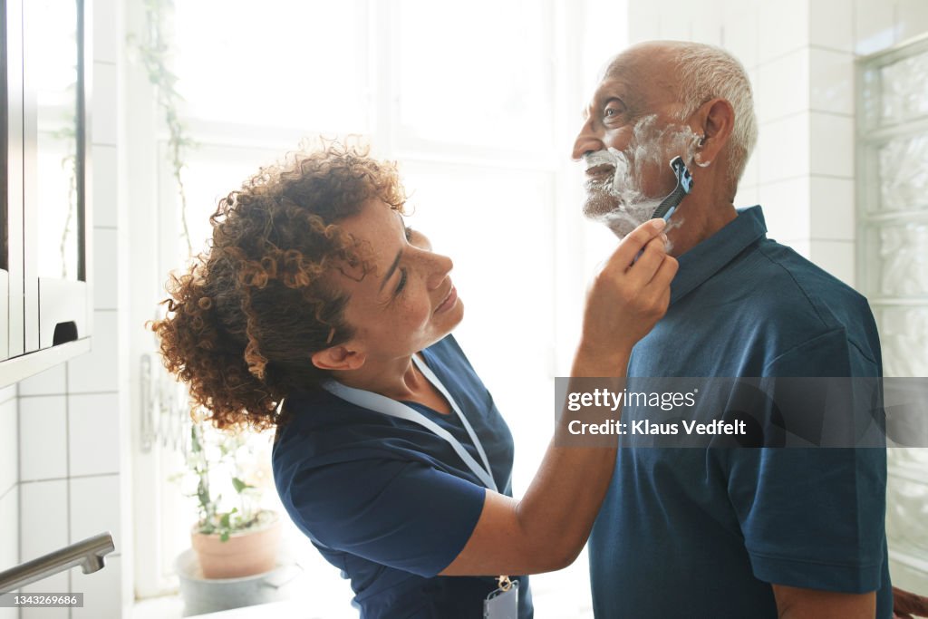 Caregiver helping retired senior man in shaving