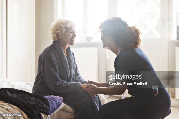 female caregiver holding hands of senior woman - affettuoso foto e immagini stock
