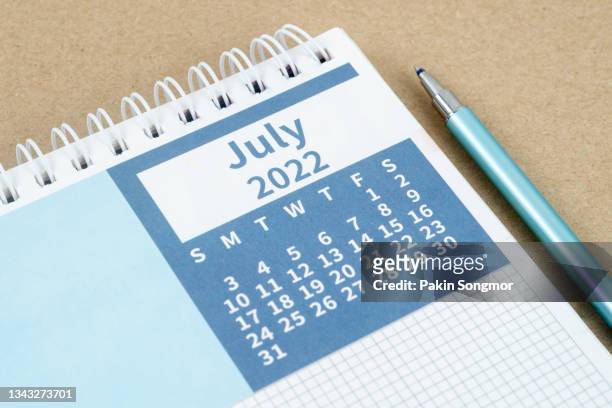 calendar desk 2022 on july month, top view calendar planning and pen on gray paper background. - july stock pictures, royalty-free photos & images