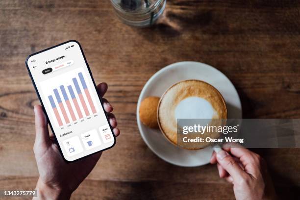 close up shot of woman checking and adjusting energy usage on smartphone at home - energy efficient home ストックフォトと画像