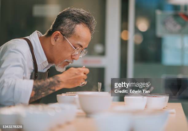 professional asian chinese senior man barista connoisseur performing coffee cupping tasting coffee cupping with spoon - examining food stock pictures, royalty-free photos & images