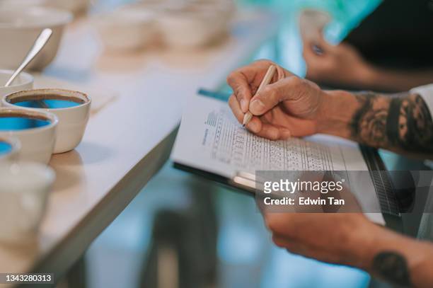 close up professional asian chinese barista connoisseur performing coffee cupping writing down on clipboard after tasting coffee cupping - taste test stock pictures, royalty-free photos & images