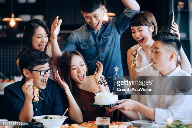 a young group of joyful friends celebrating at a birthday party together. friends cheering and surprising the birthday girl with a birthday cake during party - birthday surprise stock pictures, royalty-free photos & images