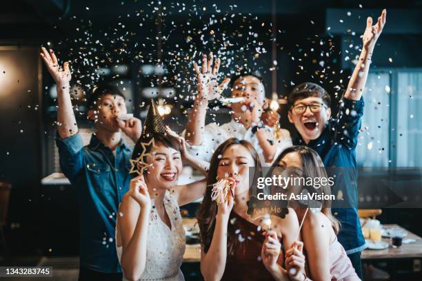 陽気なアジアの男女の若いグループは、小道具を楽しんで、パーティーで輝く紙吹雪を吹く - 小道具 ストックフォトと画像