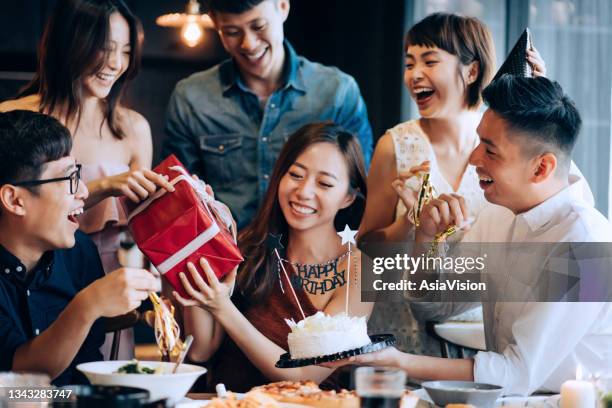 un jeune groupe d’amis joyeux célébrant ensemble lors d’une fête d’anniversaire. des amis acclament et surprennent la fille d’anniversaire avec un gâteau d’anniversaire et un cadeau pendant la fête - cadeau danniversaire photos et images de collection