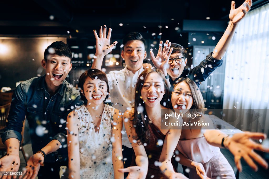 楽しいとパーティーで輝く紙吹雪を吹いている陽気なアジアの男女の若いグループ