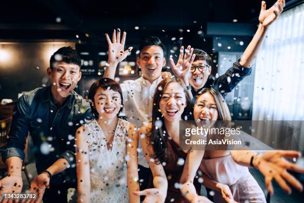 a young group of cheerful asian man and woman having fun and blowing sparkling confetti at party - asia stock pictures, royalty-free photos & images