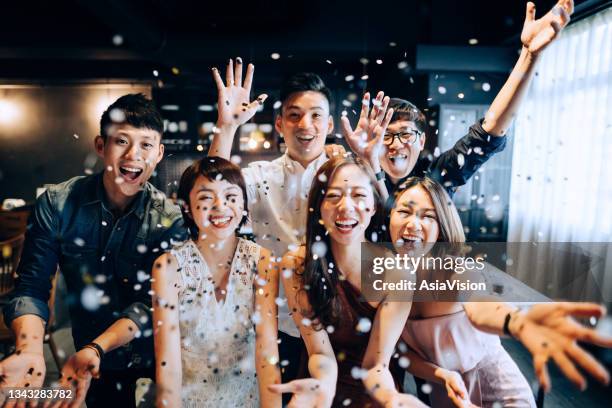 a young group of cheerful asian man and woman having fun and blowing sparkling confetti at party - etnia asiática imagens e fotografias de stock