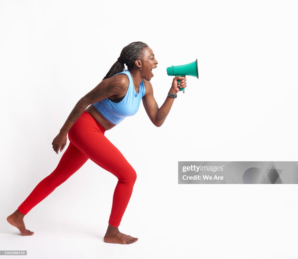 Mature woman in sports clothing lunging forward and shouting into megaphone