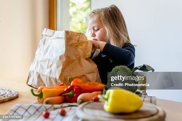 süßes mädchen entlädt gemüse aus papiertüte - young man groceries kitchen stock-fotos und bilder