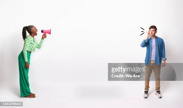 mature woman talking into a megaphone while young man holds hand to ear listening - listening stockfoto's en -beelden