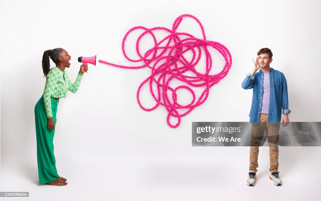 Mature woman talking into megaphone with abstract tangle of wool representing speech, young man holds hand up to ear to listen