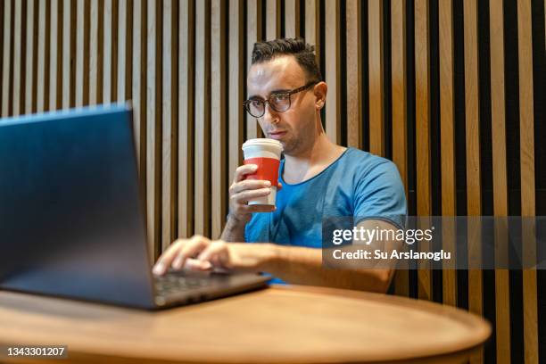 young man working with laptop whlie drinking coffee in coffee shop - whlie stock pictures, royalty-free photos & images